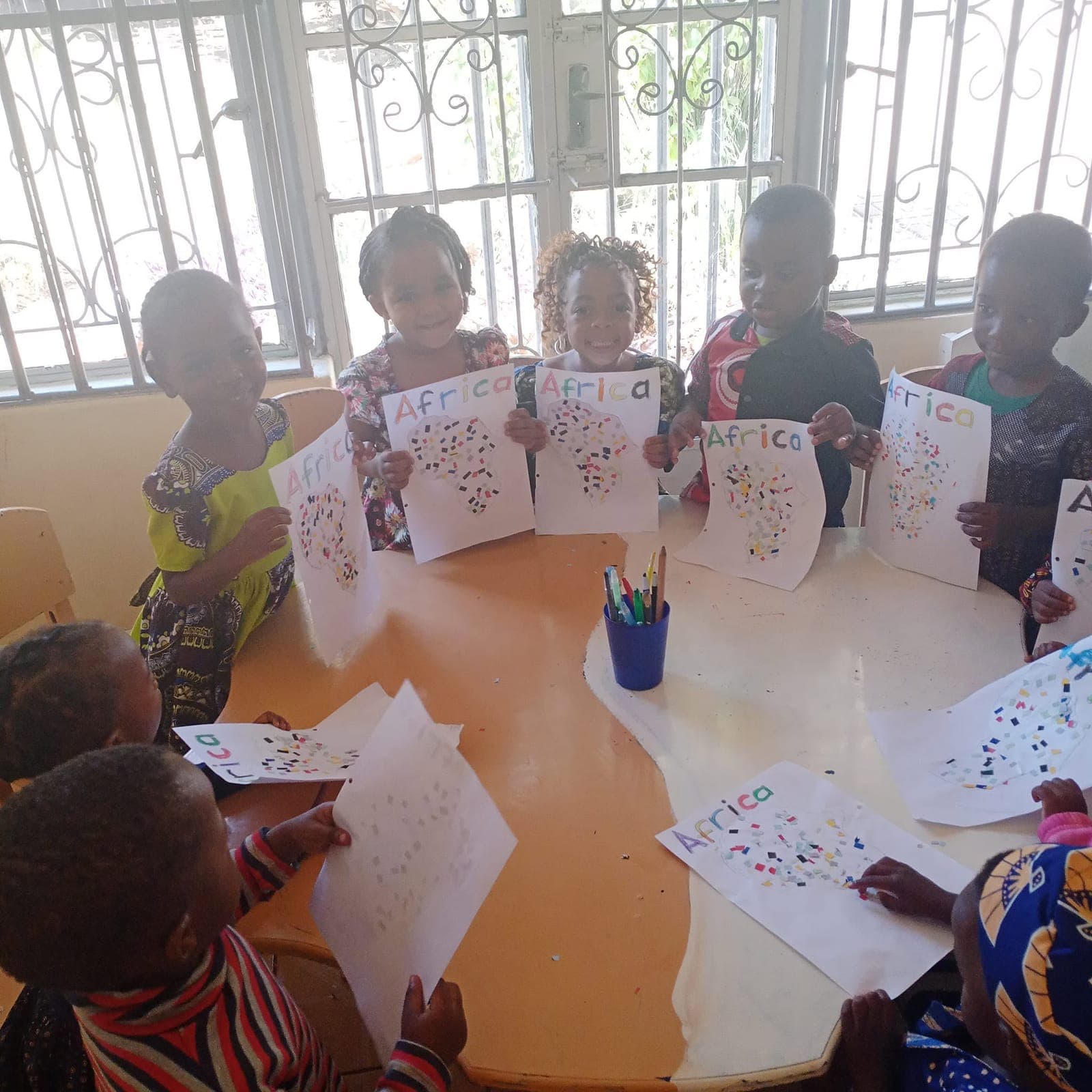 Children holding up their dot paintings around a classroom table at Nirmeen, Belvedere