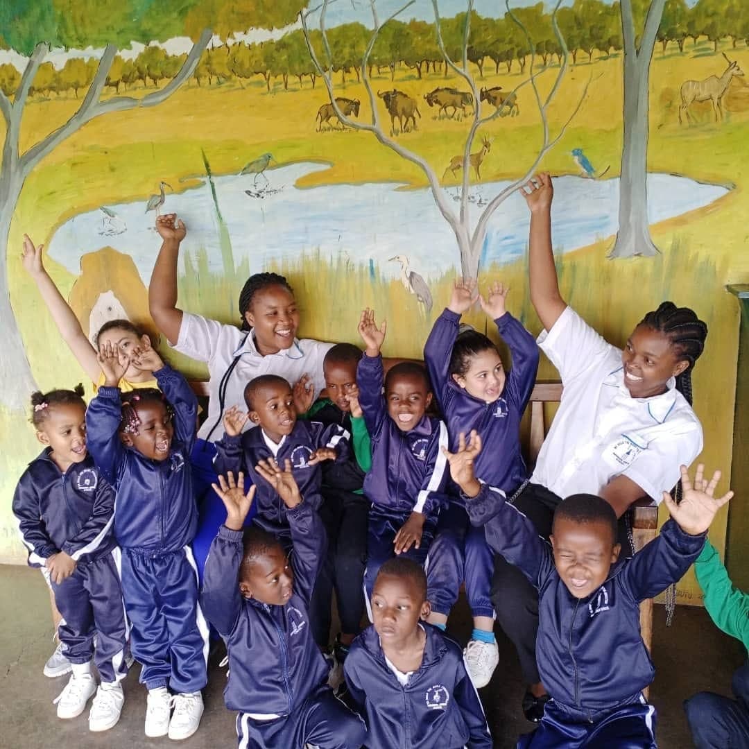 Young children waving and smiling in front of the painted mural at Nirmeen, Belvedere